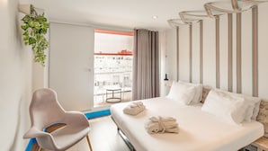 Een moderne hotelkamer met een groot bed, een stoel en een uitzicht op de stad door een glazen deur.