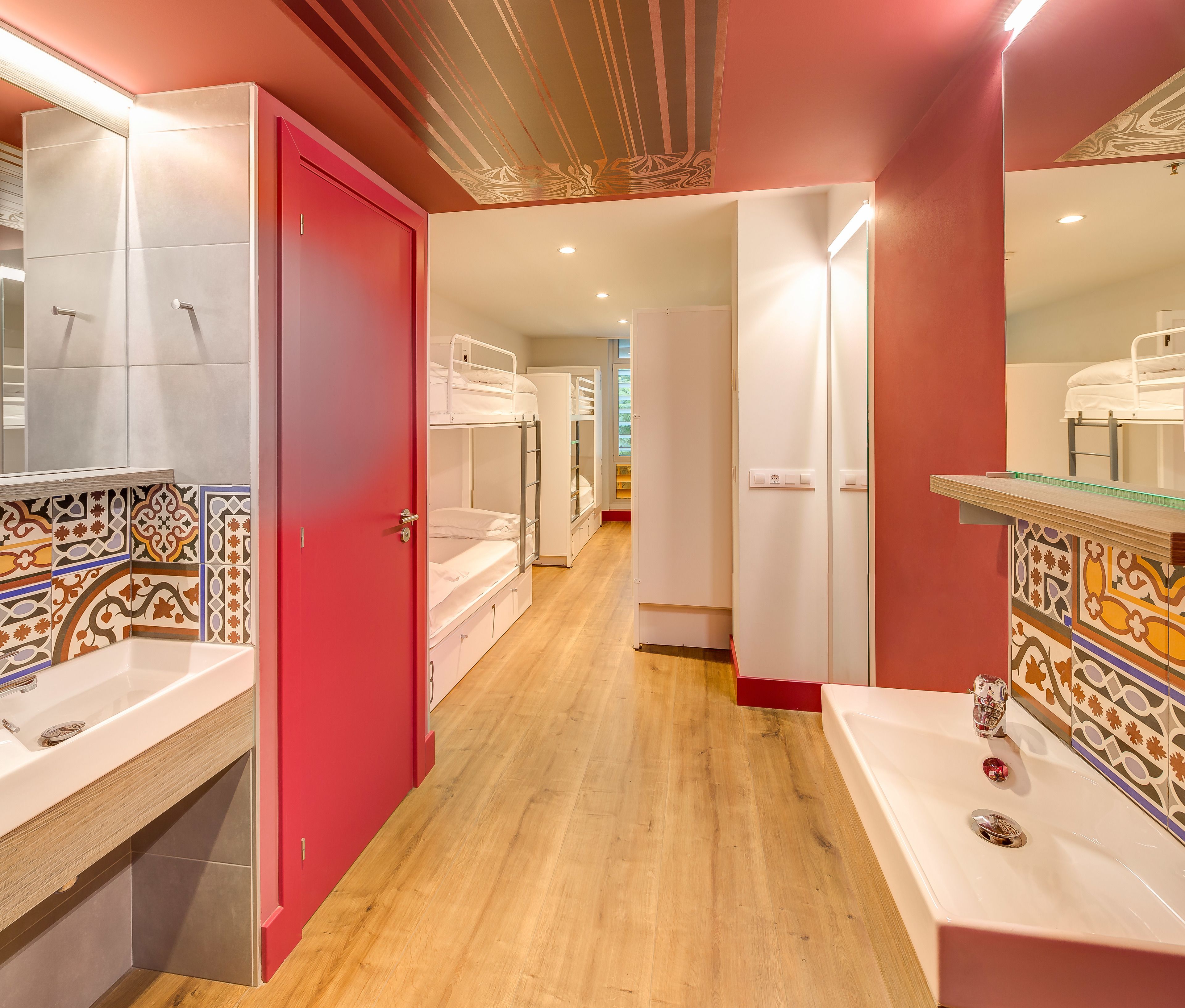 A hotel bathroom with a red door, multiple bunk beds, and a large mirror.