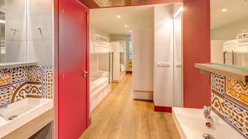 Un baño de hotel con una puerta roja, varios catres literas y un espejo grande.