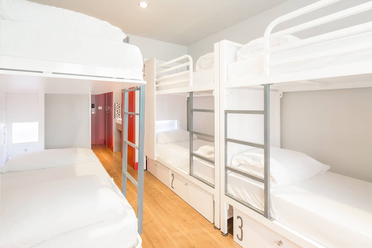 A dormitory room with bunk beds, wooden flooring, and a red door.
