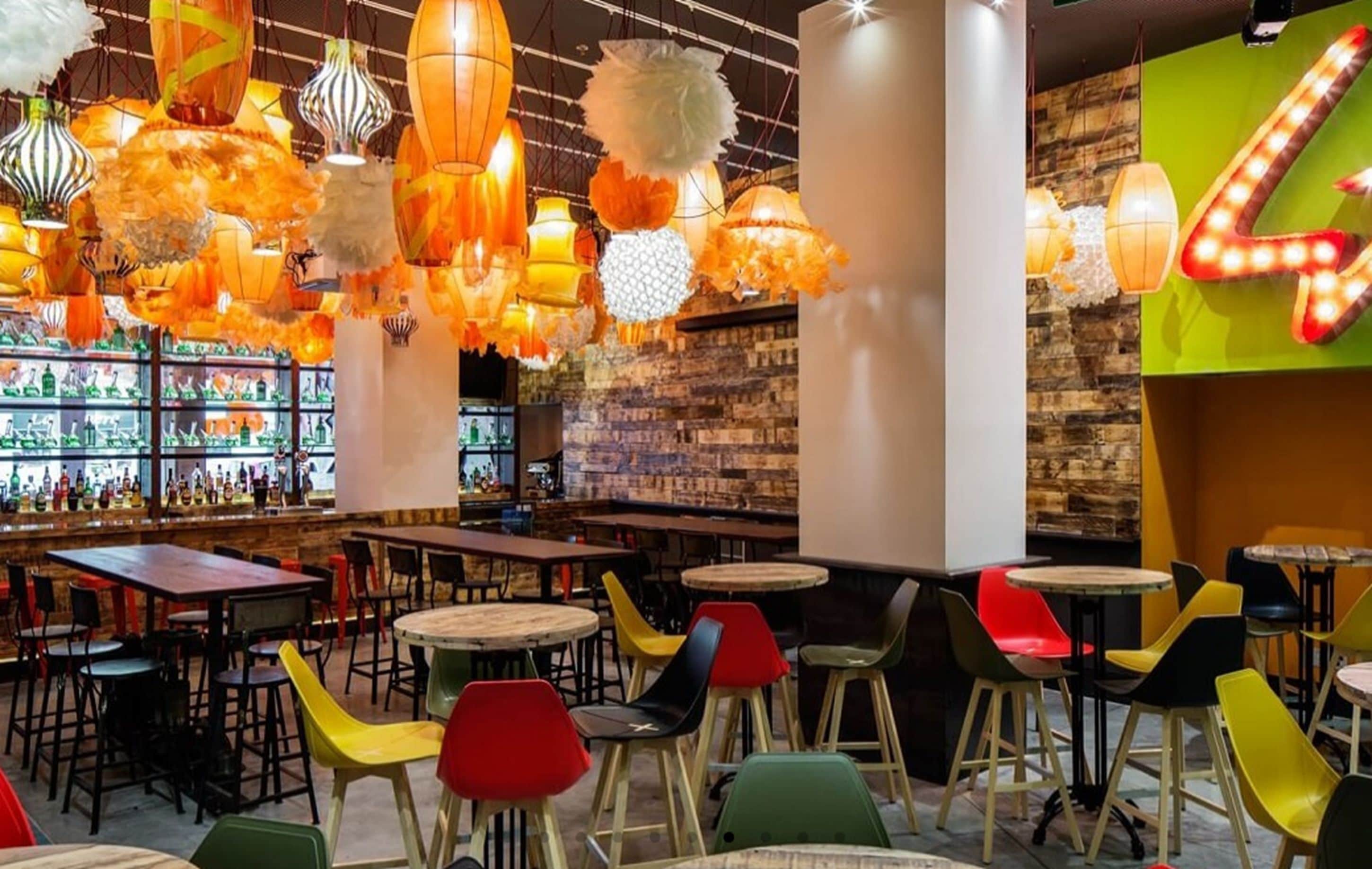 Zona de bar con sillas coloridas y lámparas colgantes.