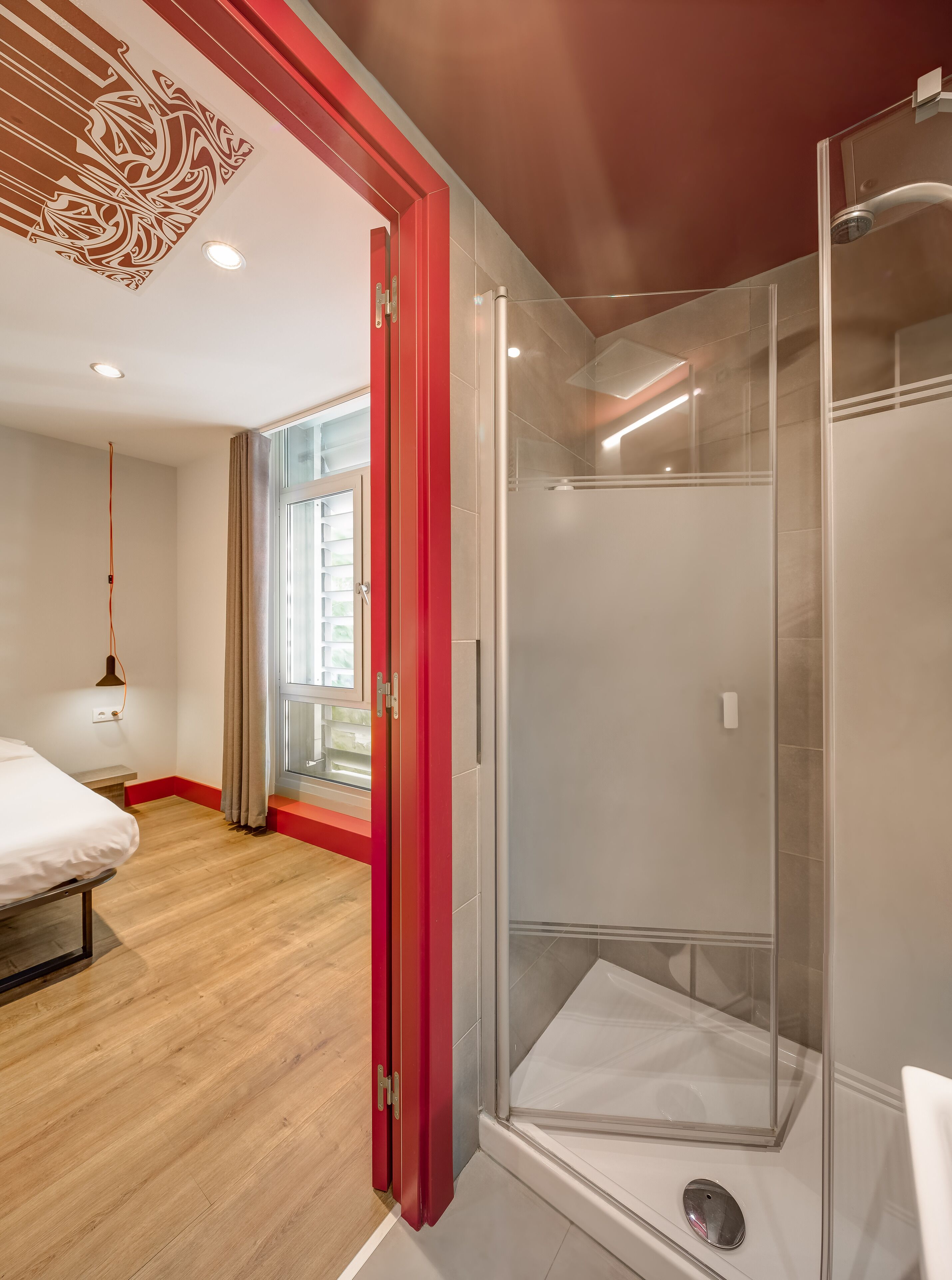 Un baño moderno con cabina de ducha de vidrio, suelo de madera y una cama en la habitación contigua.