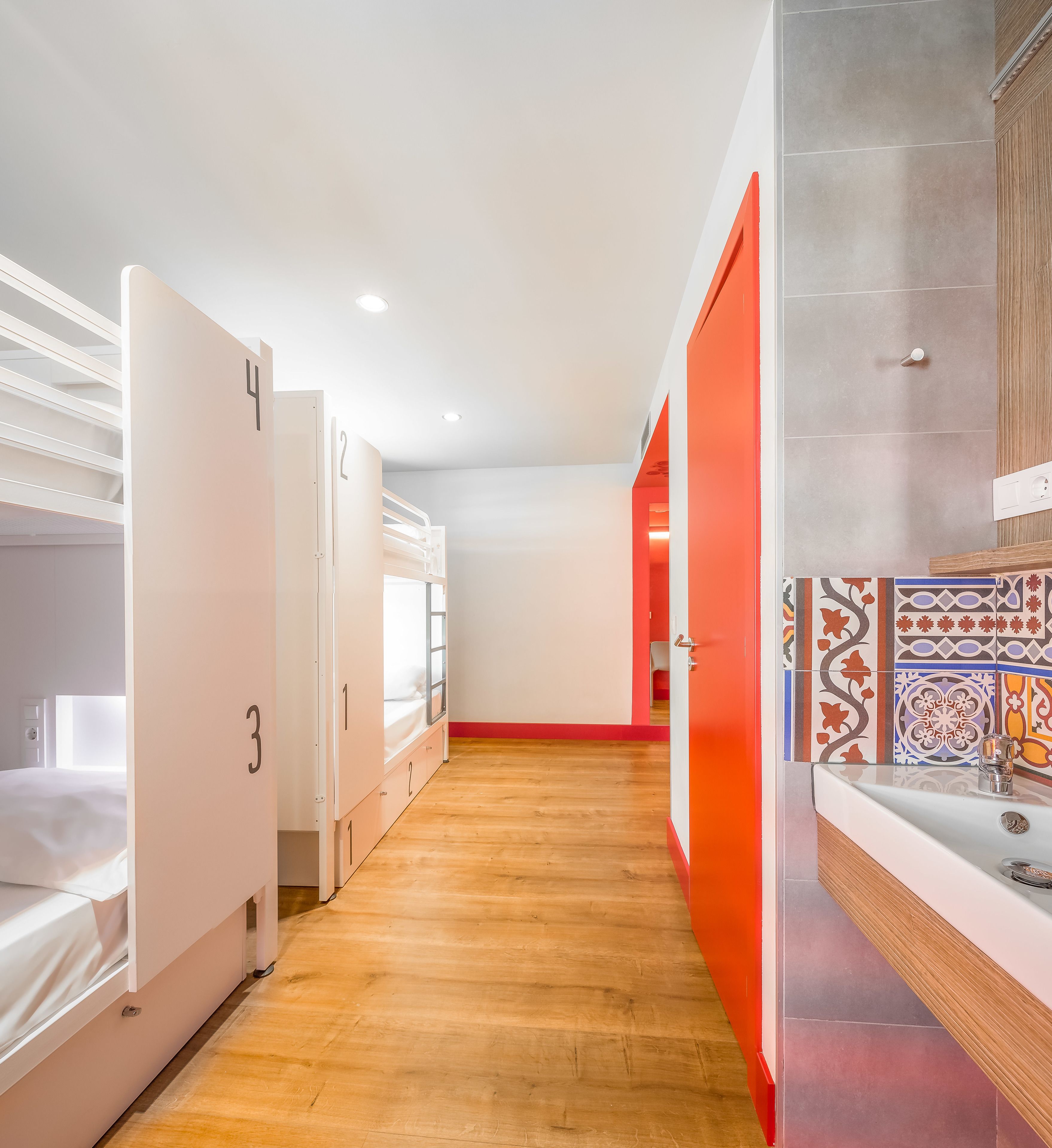A hotel corridor with bunk beds, a red door, and a tiled wall.