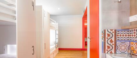 A hotel corridor with bunk beds, a red door, and a tiled wall.