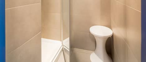 Un baño moderno con cabina de ducha de vidrio, inodoro blanco y azulejos color beige.