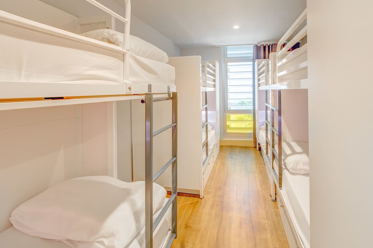 A narrow corridor with bunk beds on both sides, leading to a bright window.