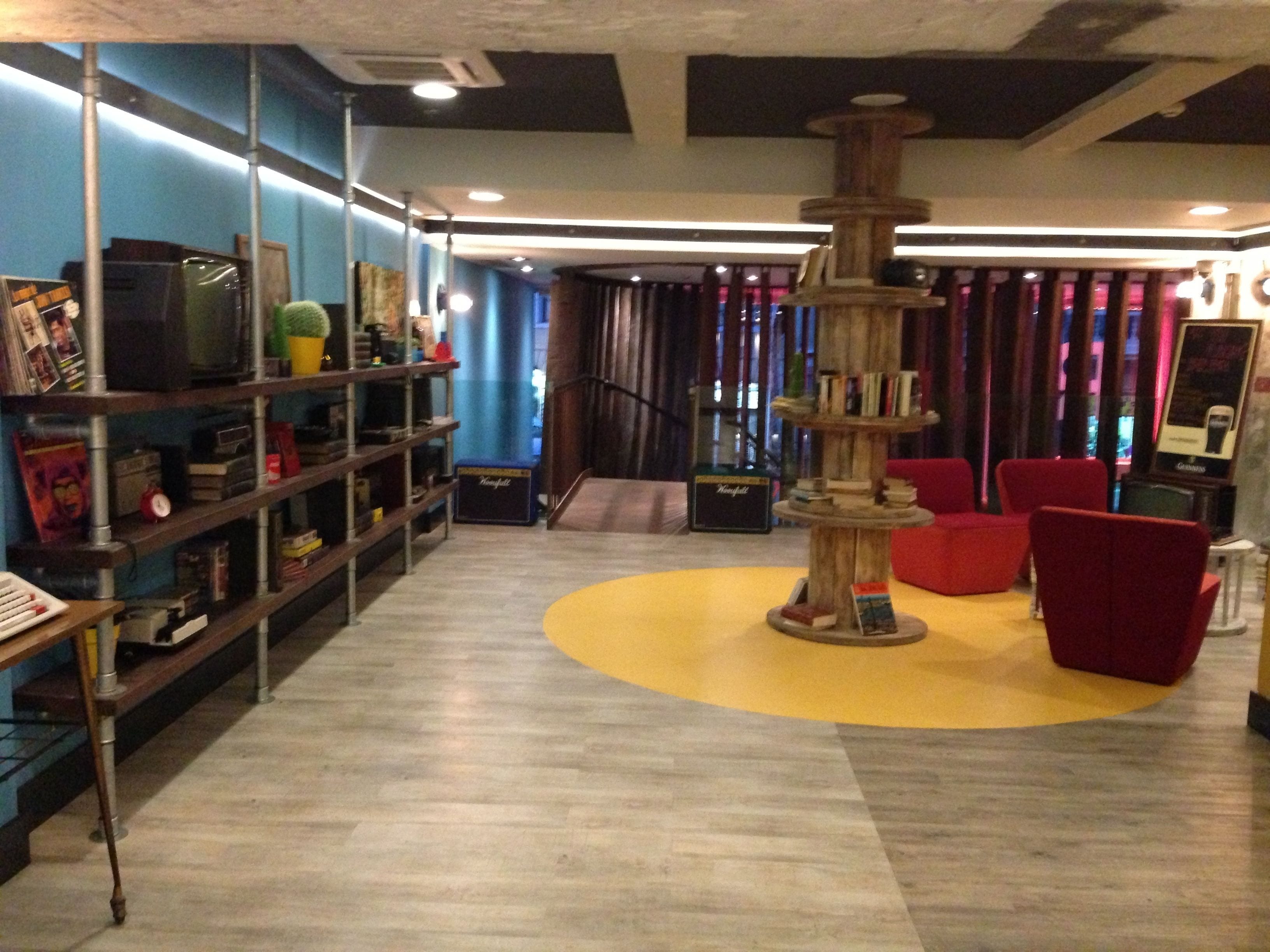 Un interior moderno con una estructura central de madera, estantes con libros y objetos decorativos, y sillas rojas.