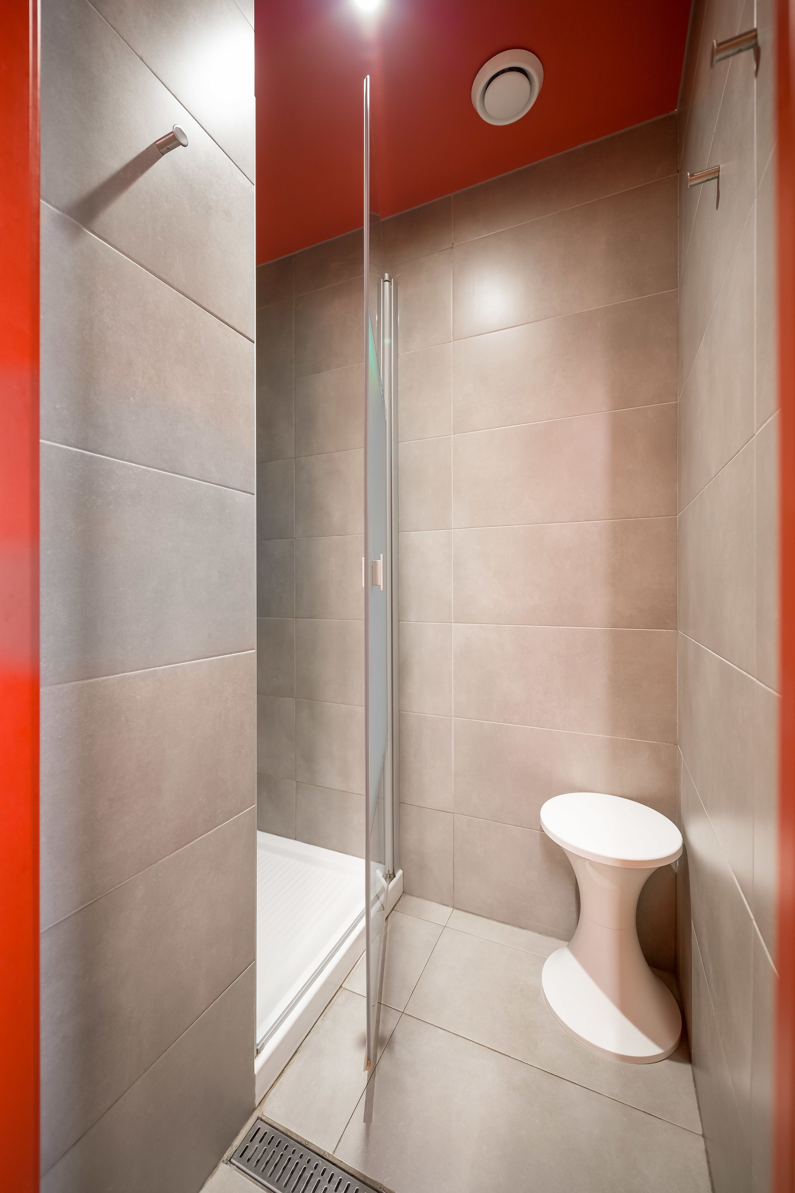 A modern bathroom with a glass shower enclosure, a white toilet, and a red accent wall.