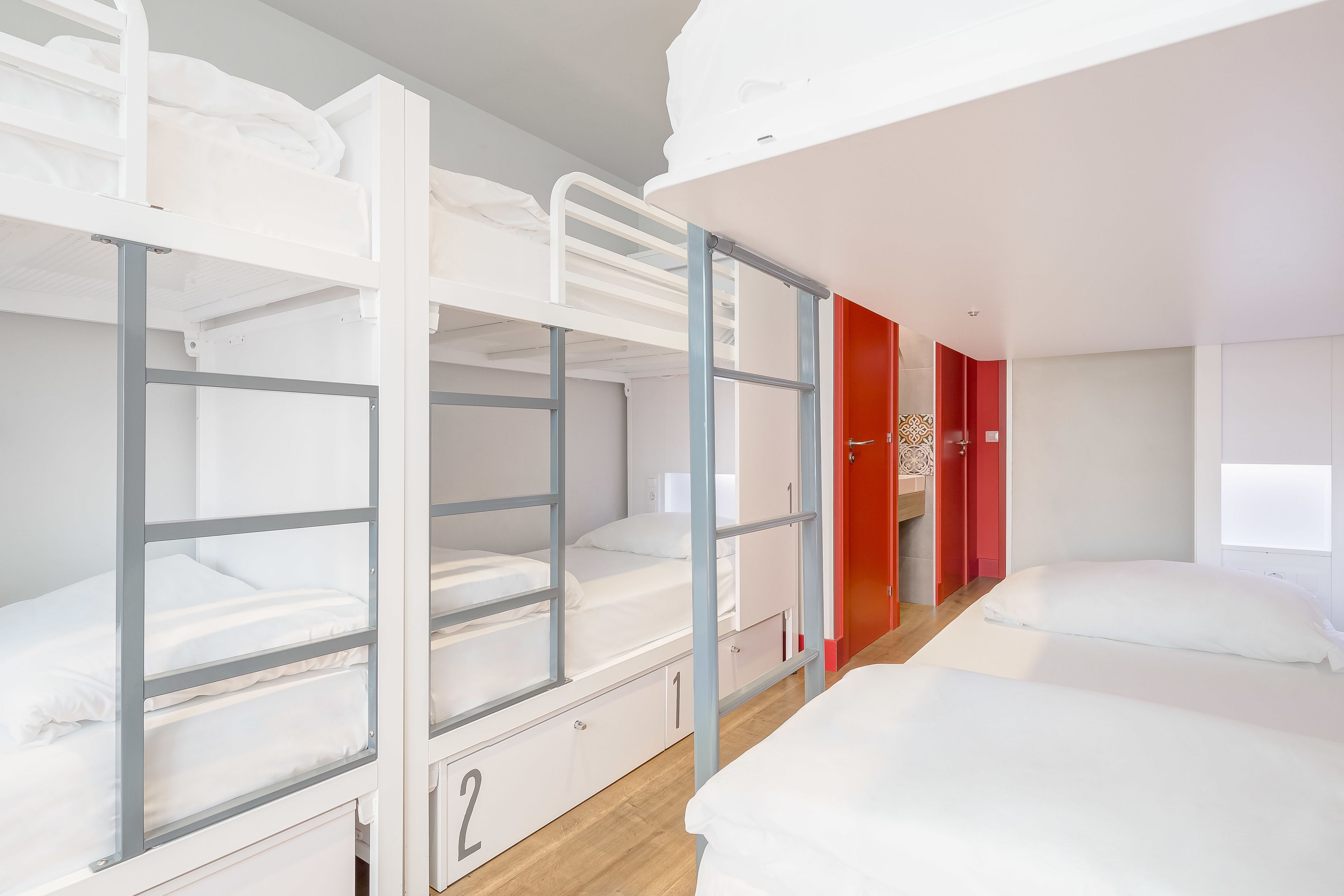 Une chambre de dortoir avec des lits superposés, une porte rouge et une fenêtre.