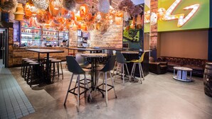 Een barruimte met meerdere tafels en stoelen, een bakstenen muur en een neonreclame.