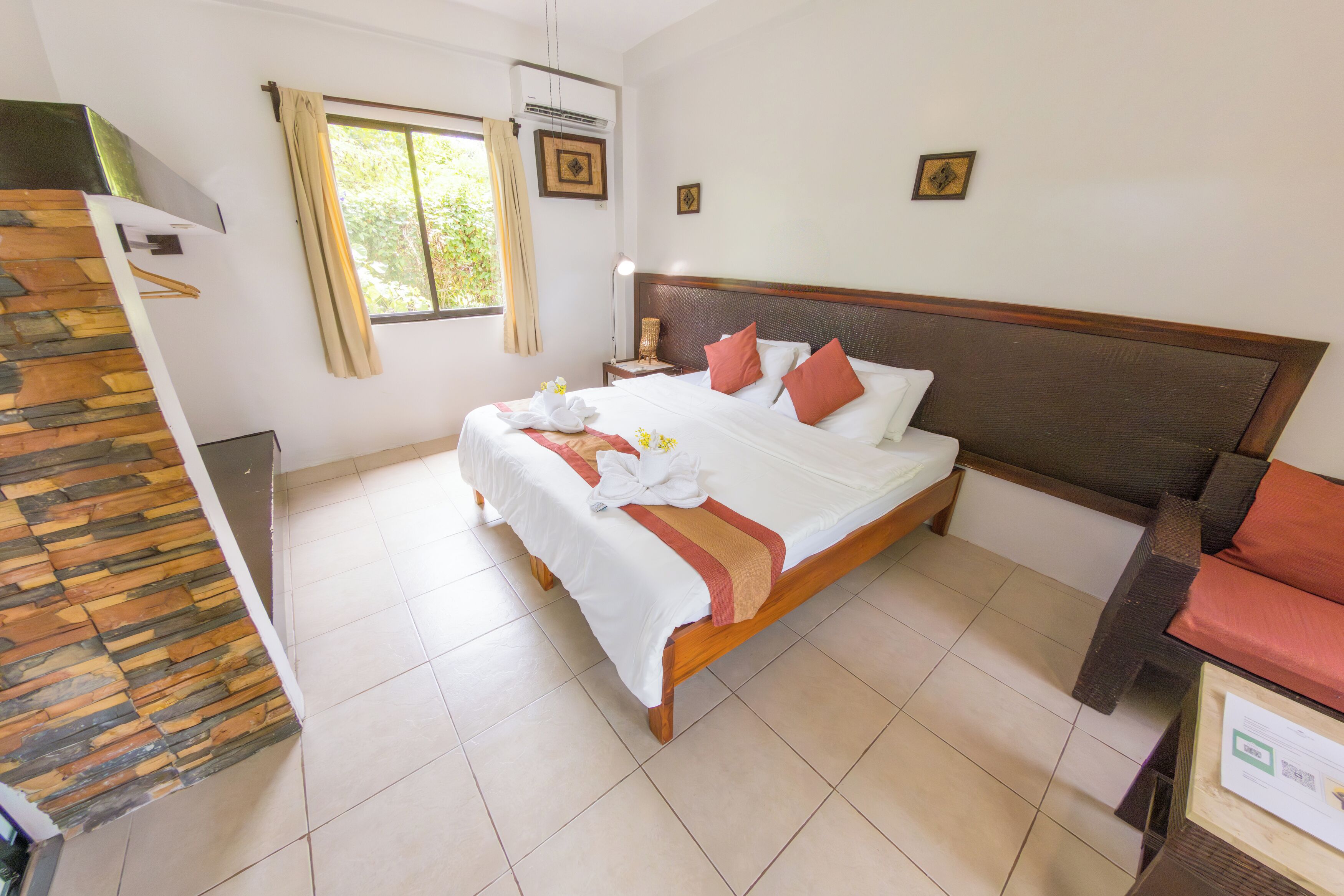 Ein Hotelzimmer mit einem großen Bett, einem Holzkopfende, einem Nachttisch, einem Schreibtisch, einem Sessel, einem Fenster mit Vorhängen und einer Treppe mit Holzwand.
