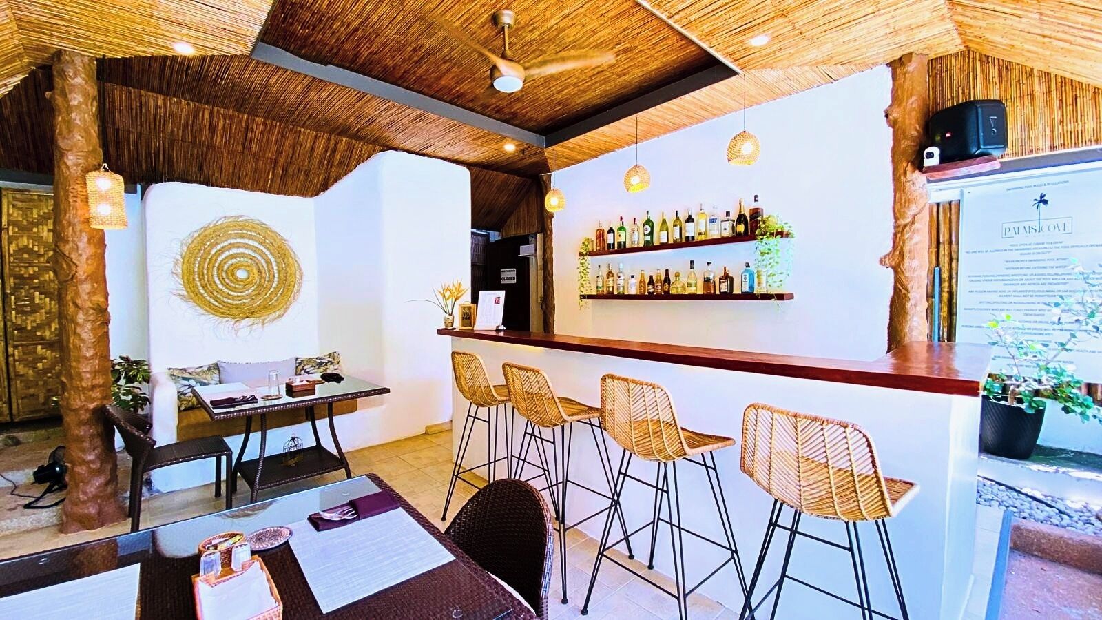 Eine Bar mit Korbstühlen, Holzbalkendecke und einer an der Wand befestigten Spirituosenregal.