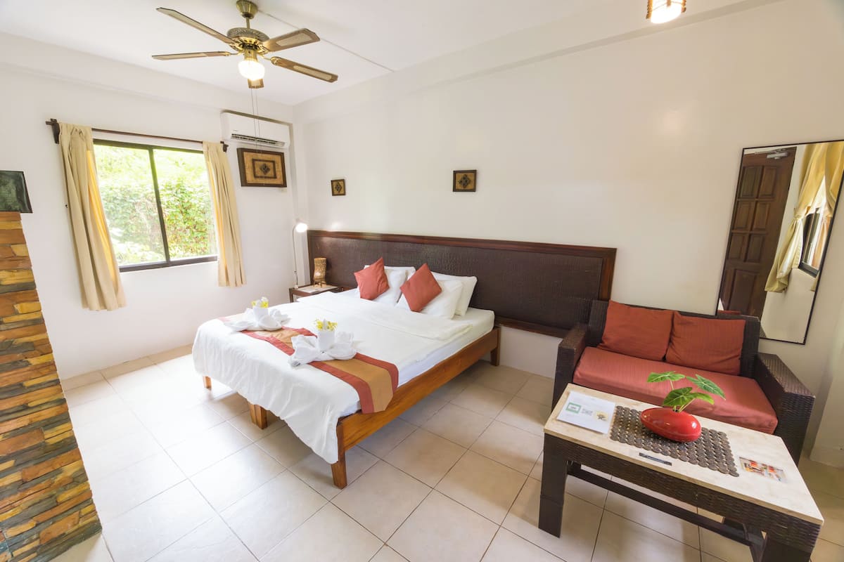 A hotel room with a bed, a sofa, a table with a plant, and a ceiling fan.