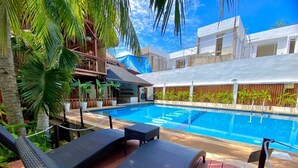 A poolside area with lounge chairs, a pool, and a wooden deck. - Palms Cove Resort (Panglao)