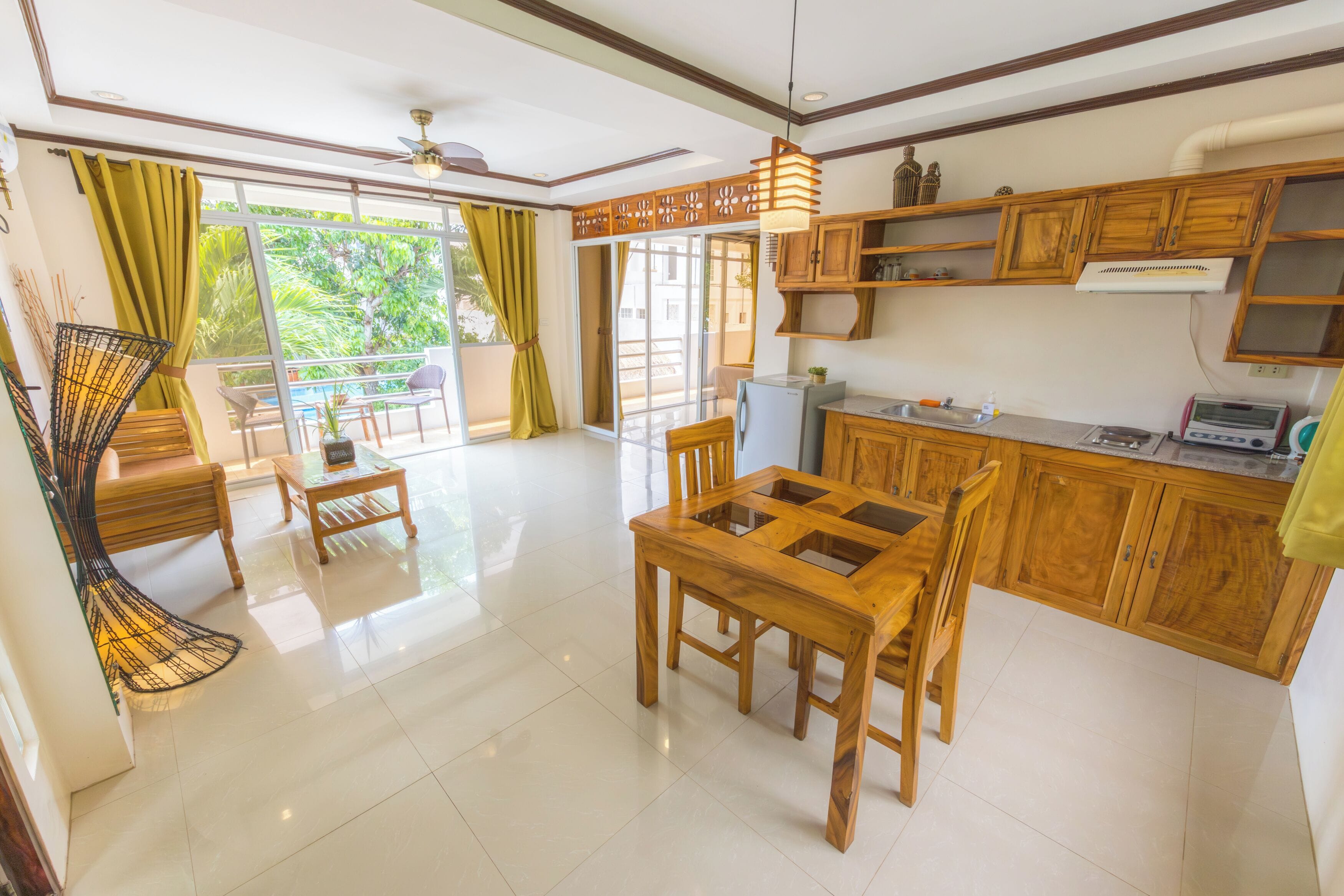 A spacious living area with a wooden dining table, chairs, and a balcony with a view of greenery.
