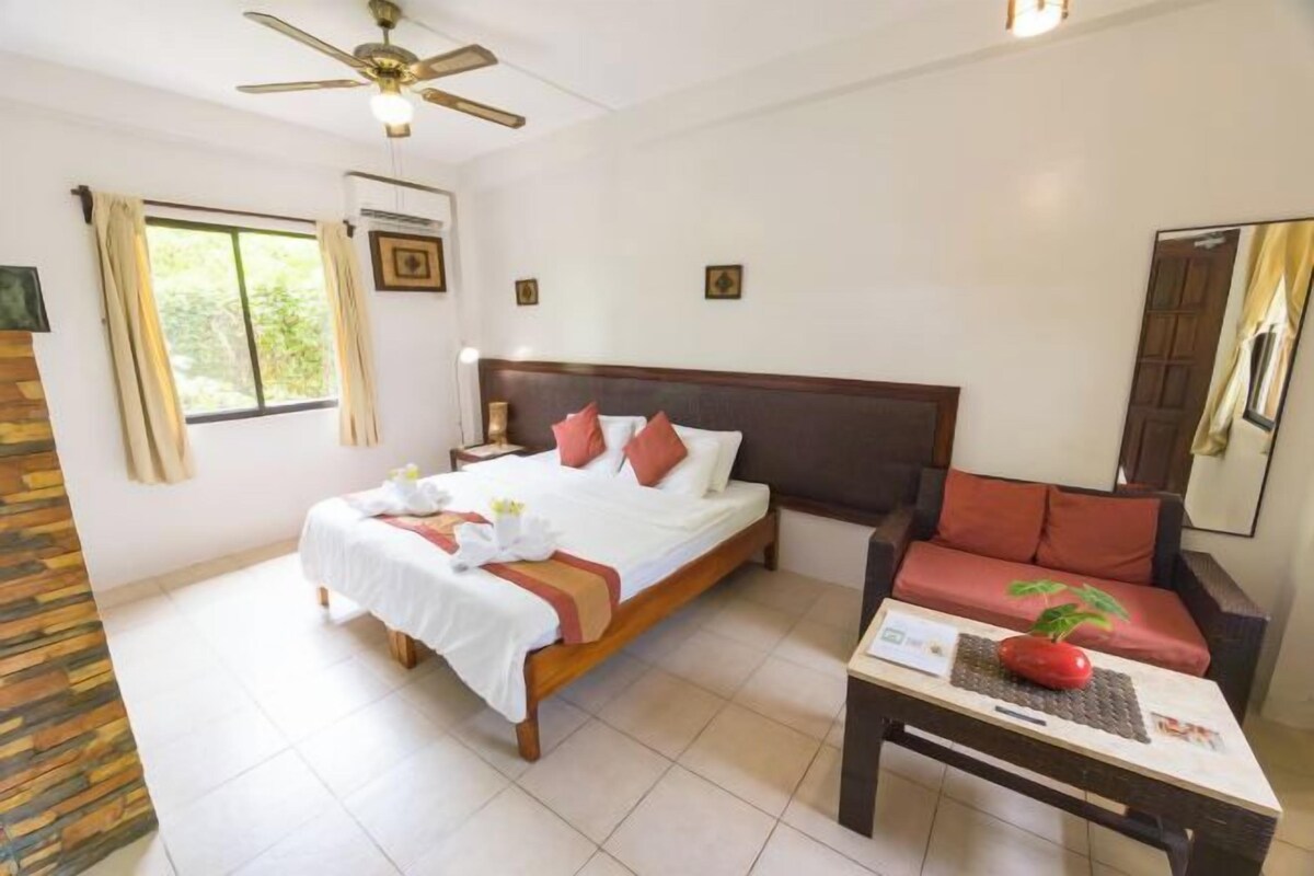 Una habitación de hotel con una cama, un sofá, una mesa con una planta y un ventilador de techo.