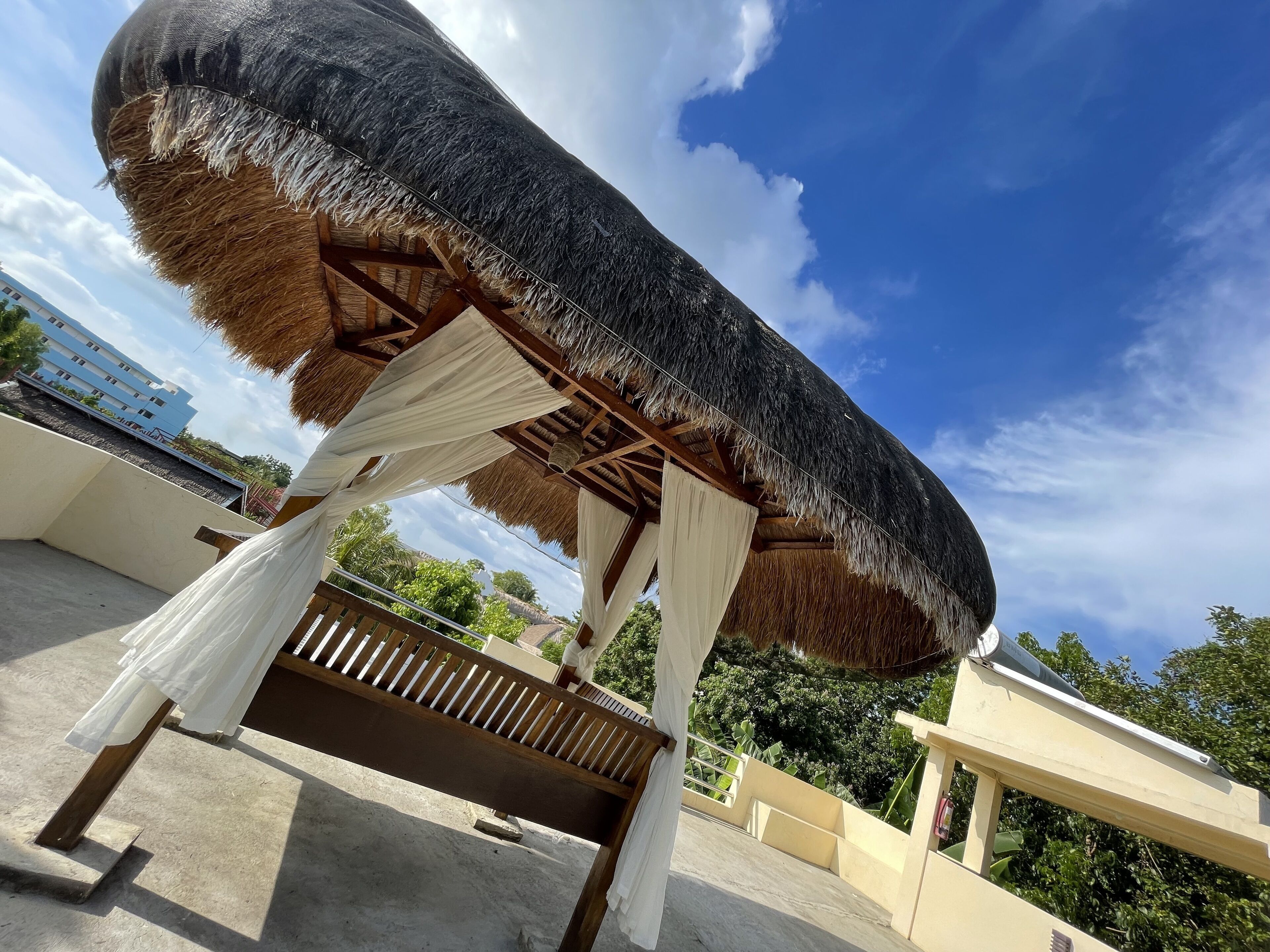 A thatched roof structure with white drapes, wooden beams, and a concrete floor.