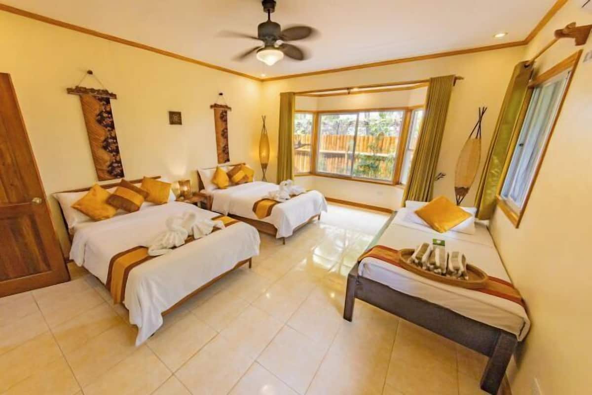 A hotel room with two beds, a ceiling fan, a window with a view, and a wooden bench with towels.
