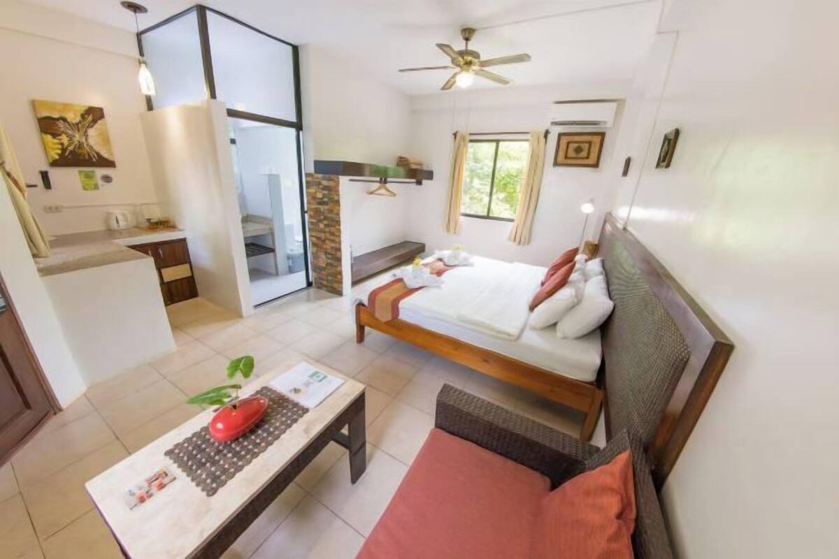 A room with a bed, a desk, a chair, a ceiling fan, and a window.