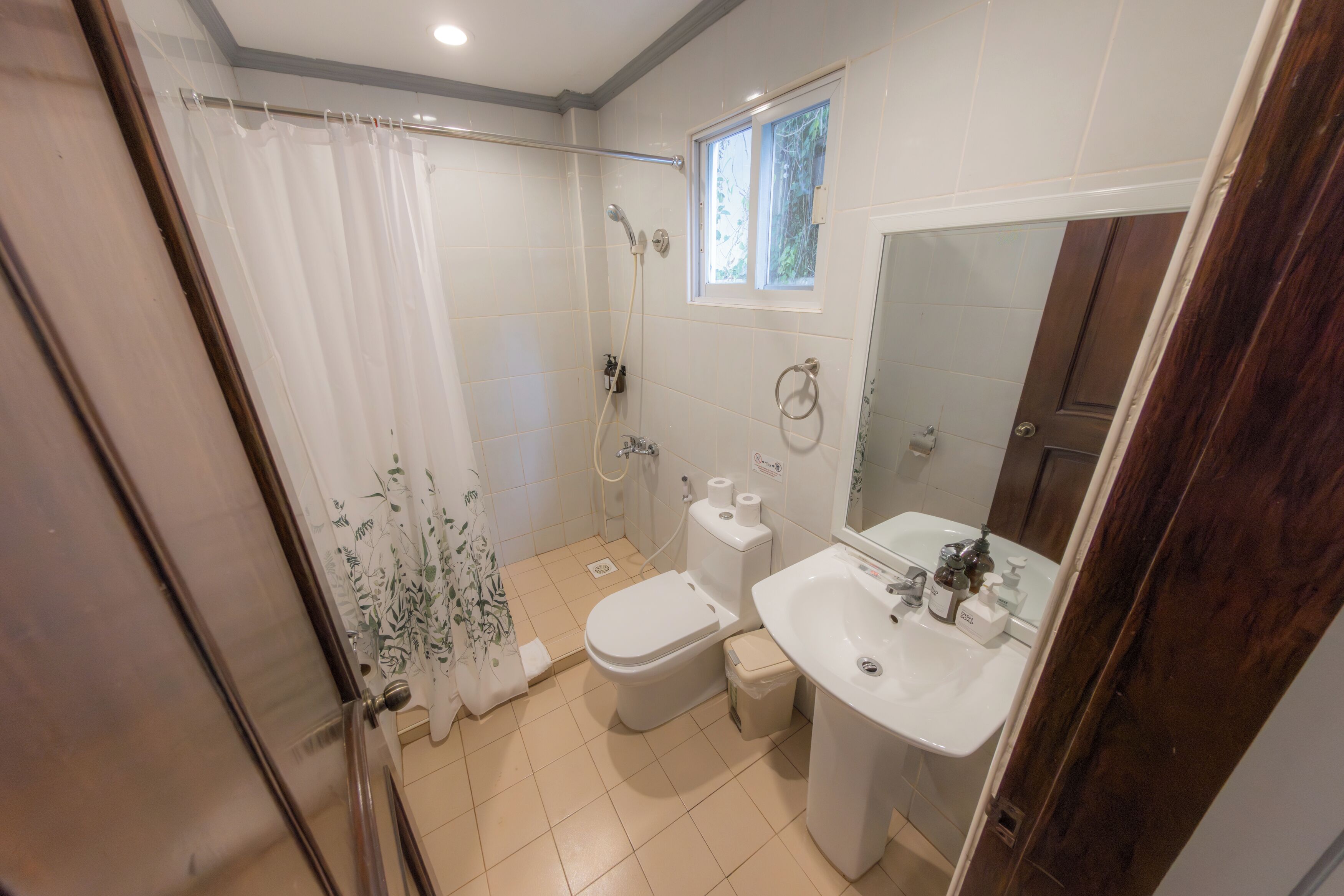 Et badeværelse med bruser, toilet, vask og et vindue.