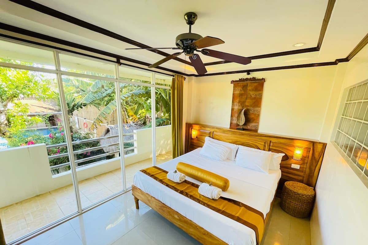 A modern bedroom with a large bed, a ceiling fan, and a view of a garden through large windows.