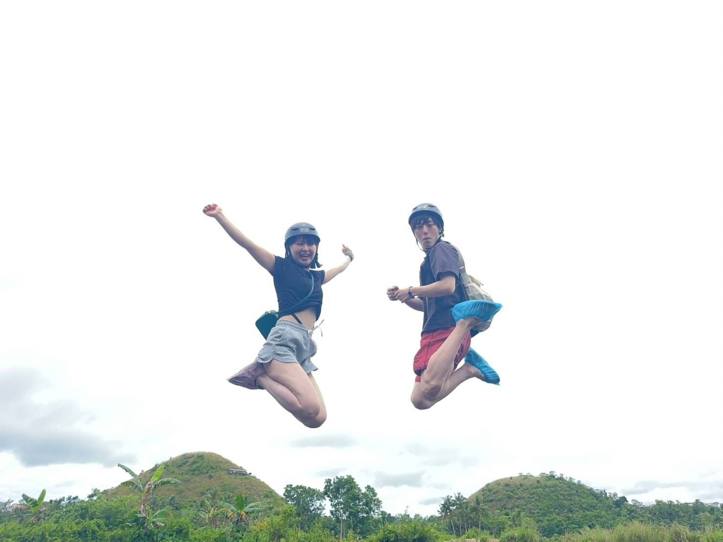 Two people jumping in the air with a hilly landscape in the background.