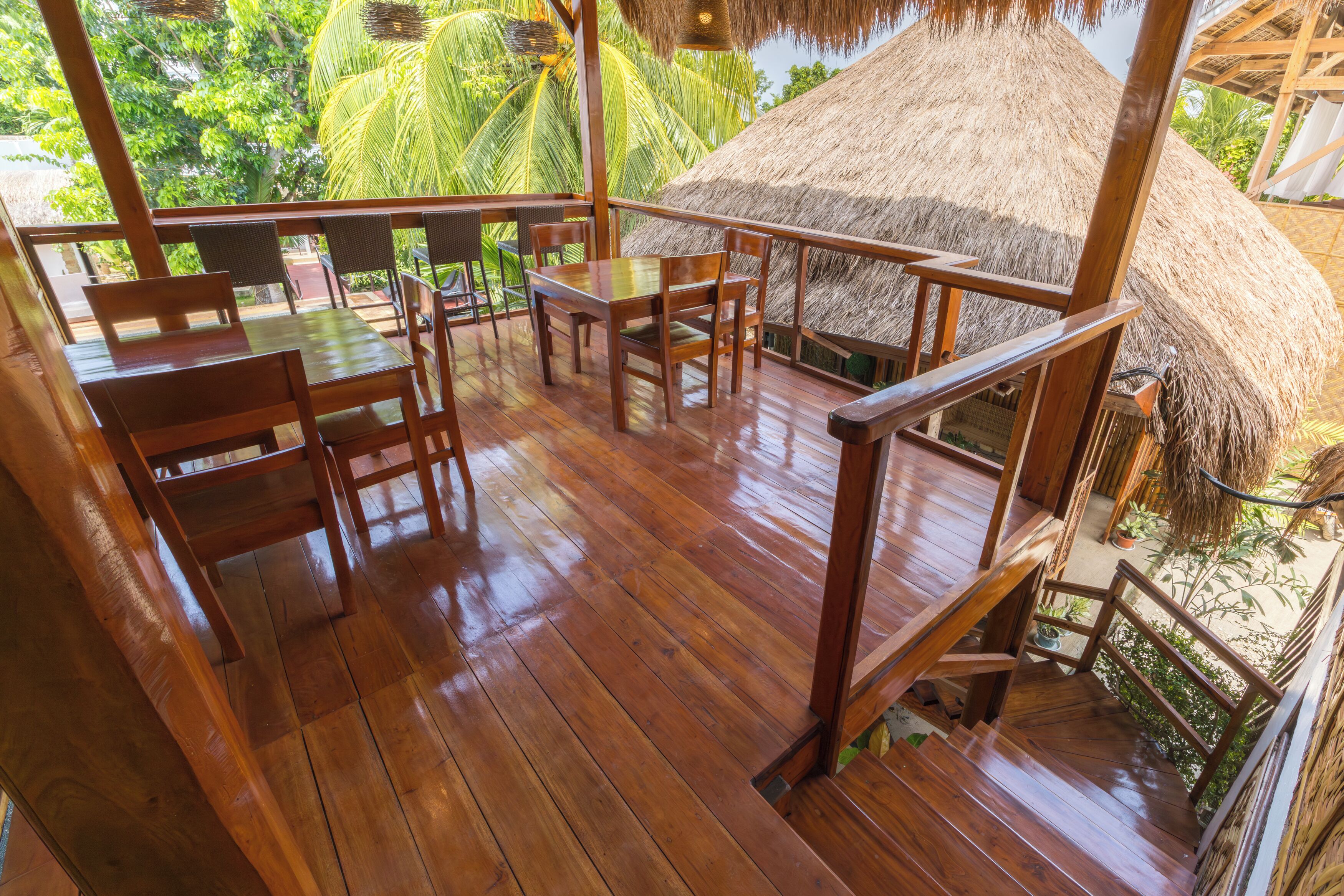 A wooden deck with a thatched-roof structure, surrounded by lush greenery.
