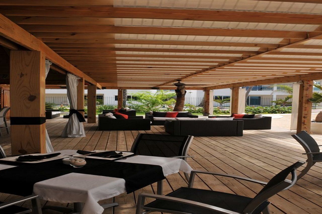 Un patio al aire libre con piso de madera, mesas con manteles blancos y sillas negras.