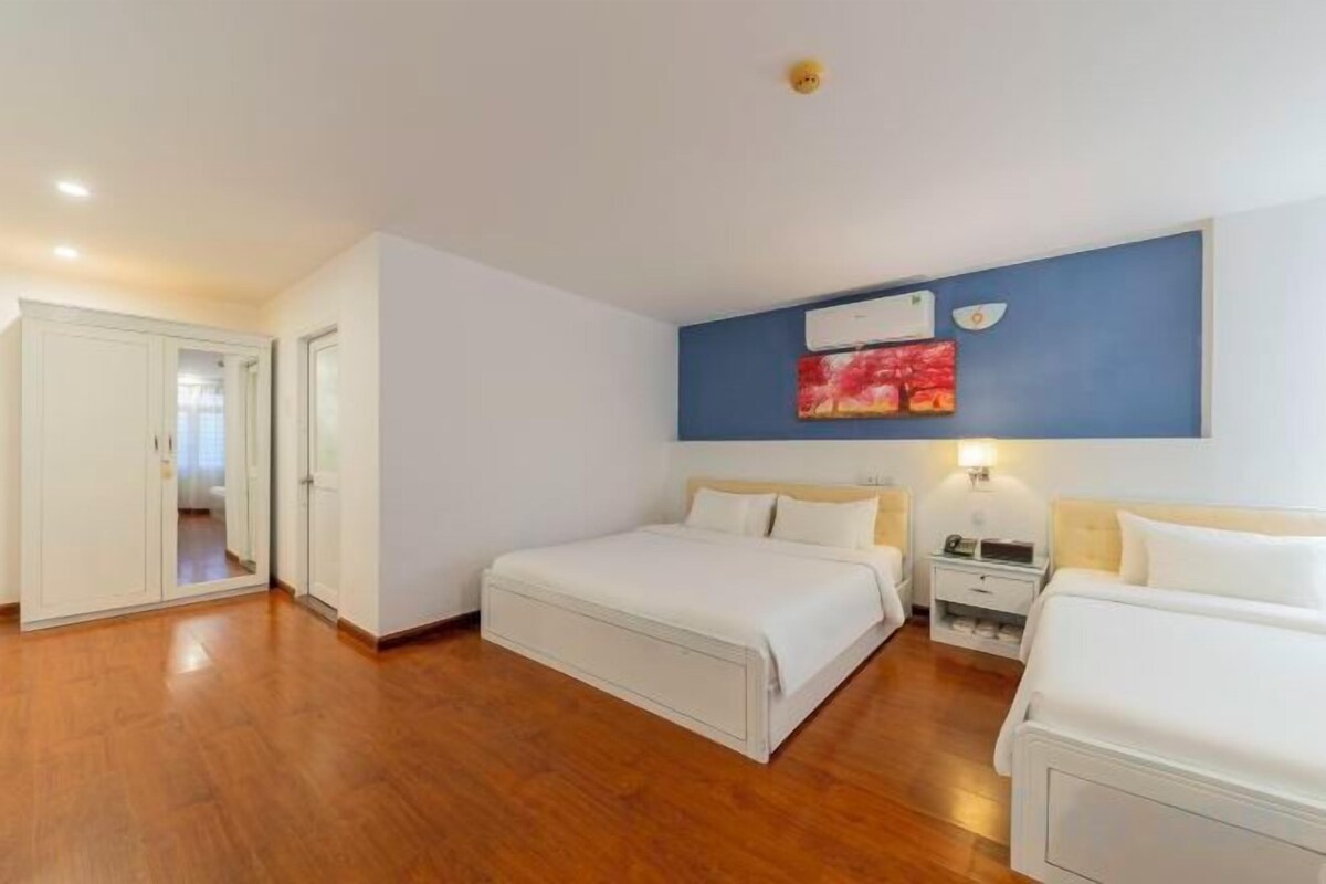 A hotel room with two beds, a wardrobe, a bedside table with a lamp, and a wall-mounted air conditioner.