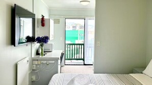 A hotel room with a bed, a television, a small table with a vase of flowers, a fire extinguisher, and a balcony with a view. - Adelaide Motel (Wellington)