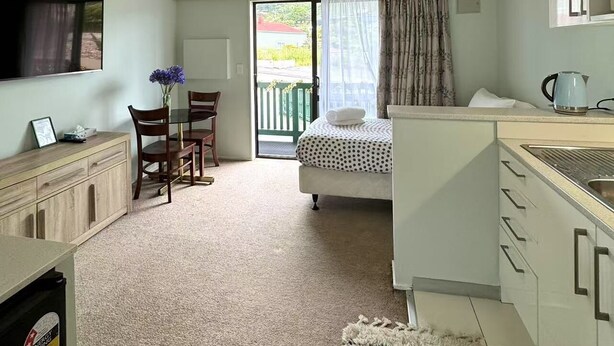 A compact room with a bed, a desk, a chair, a small table with a vase, a kettle, and a window. - Adelaide Motel (Wellington)