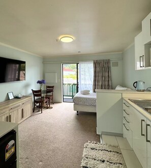 A compact room with a bed, a desk, a chair, a small table with a vase, a kettle, and a window. - Adelaide Motel (Wellington)