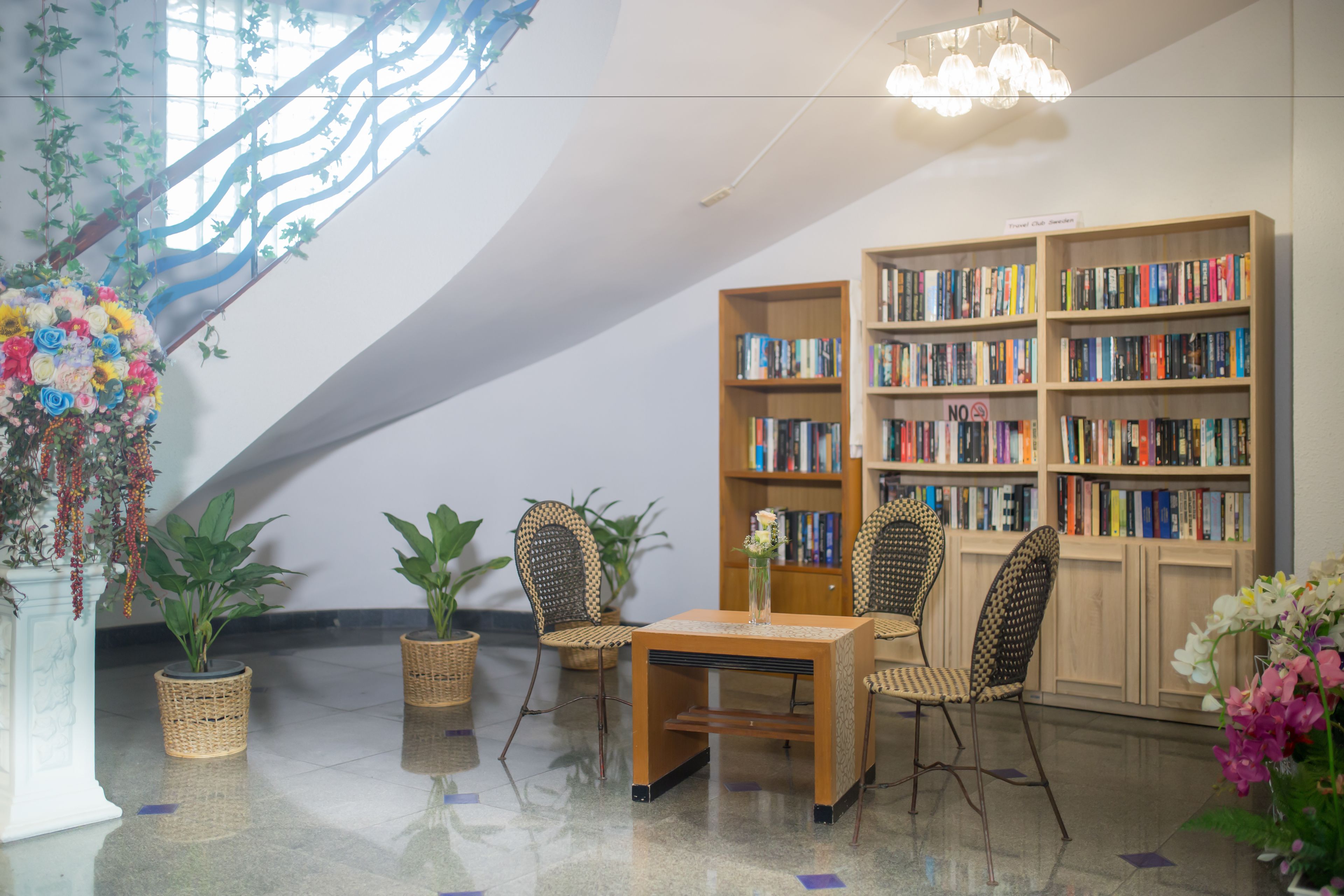Una biblioteca con estanterías, sillas de mimbre, una mesa y plantas en macetas.