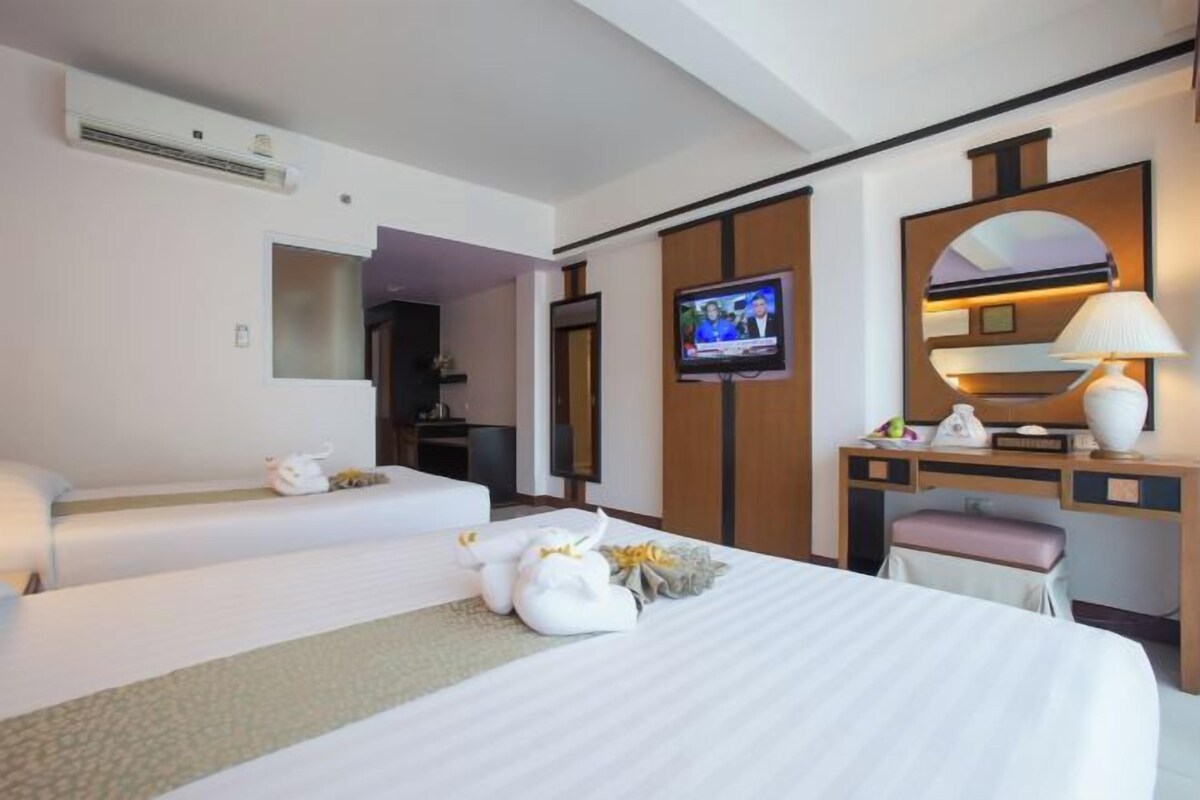 Habitación de hotel con dos camas, televisión, escritorio con lámpara y espejo.