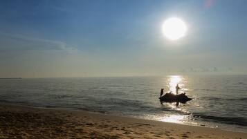 Una playa con una persona de pie en un bote en el agua, cielo despejado y el sol brillando.