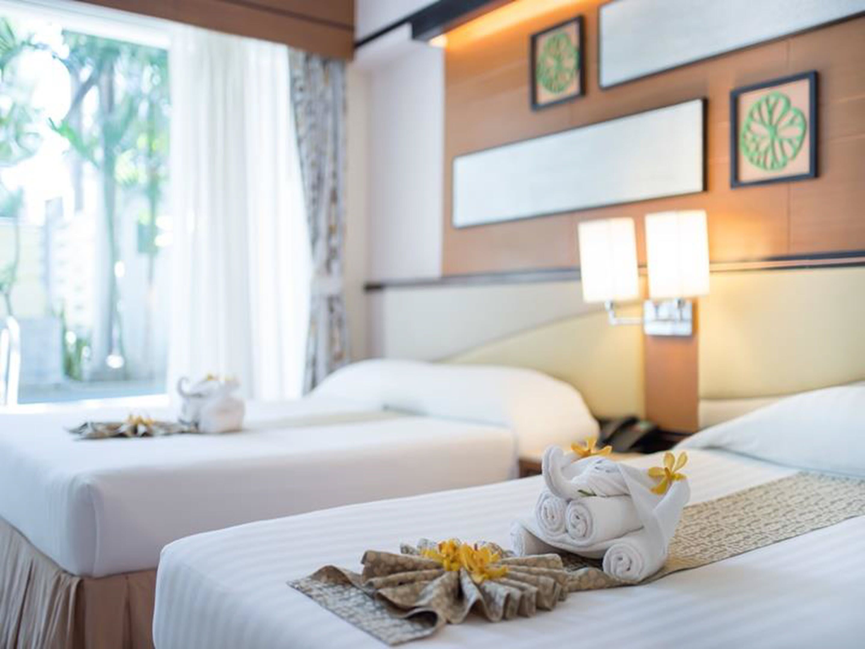 A hotel room with two beds, a window with curtains, and wall-mounted lamps.