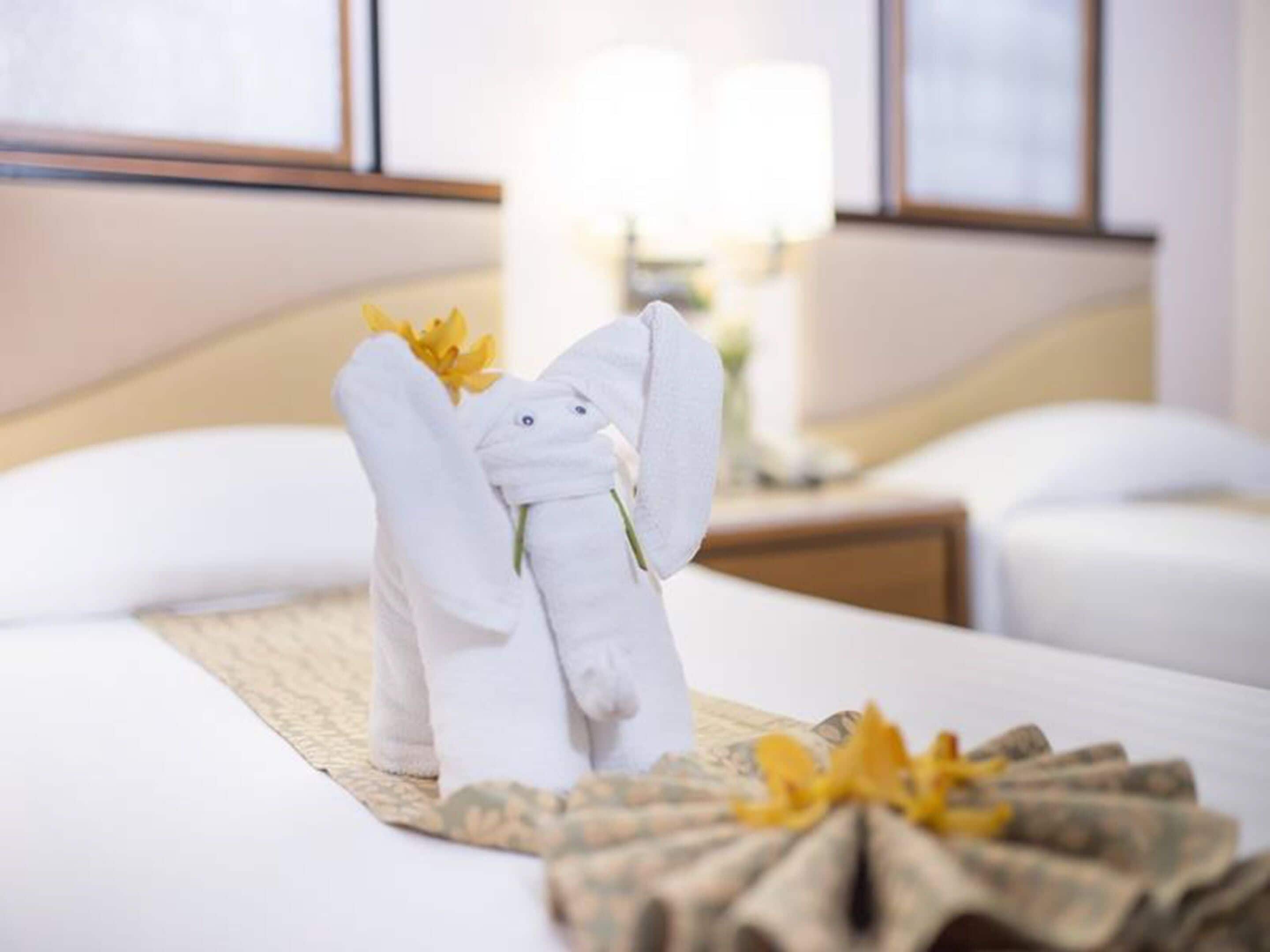 A hotel room with a neatly made bed, a decorative towel arrangement resembling a rabbit, and a floral centerpiece.