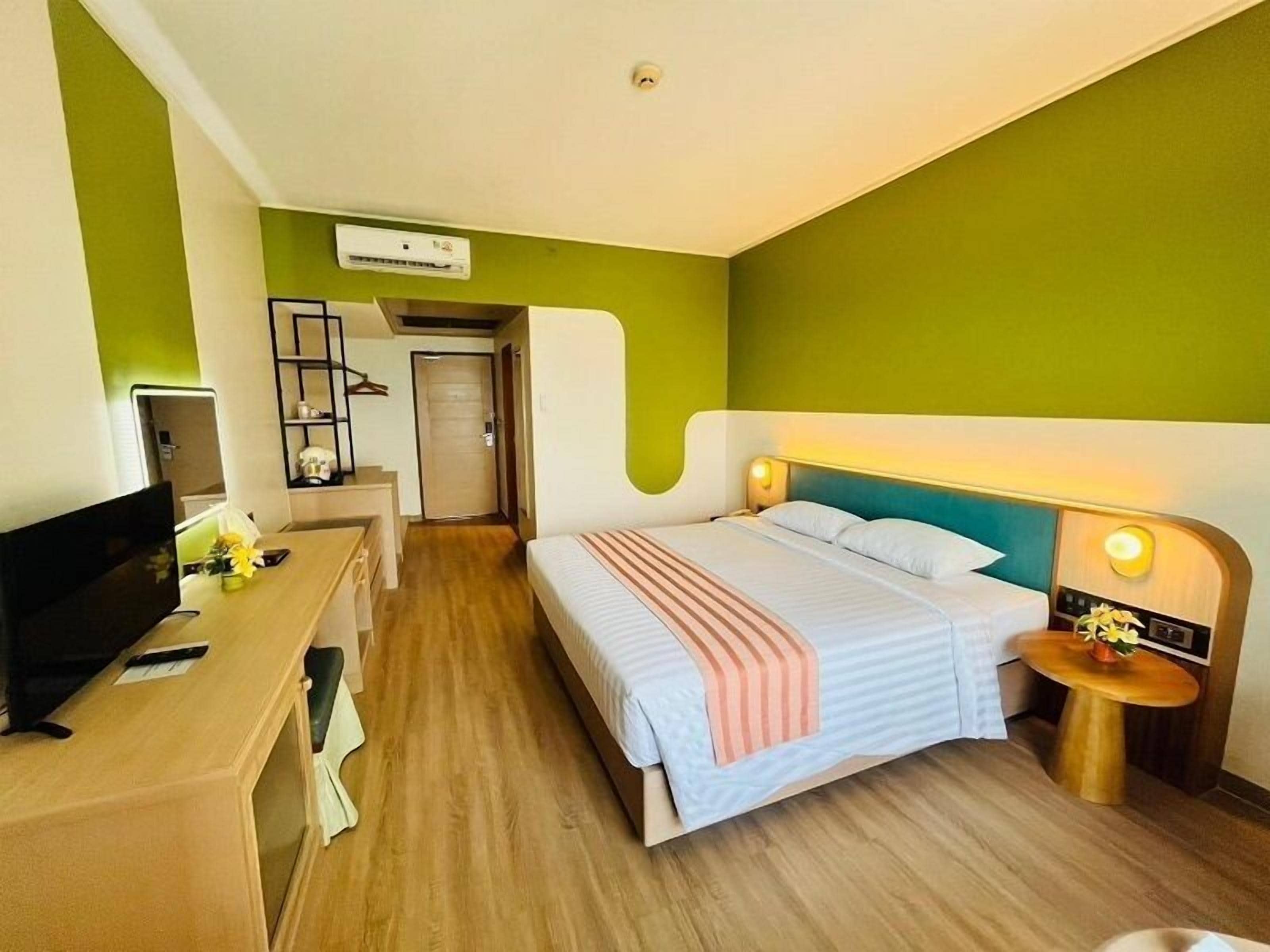 Ein Hotelzimmer mit Bett, Nachttisch, Fernseher, Schreibtisch und einer Tür zu einem weiteren Raum.
