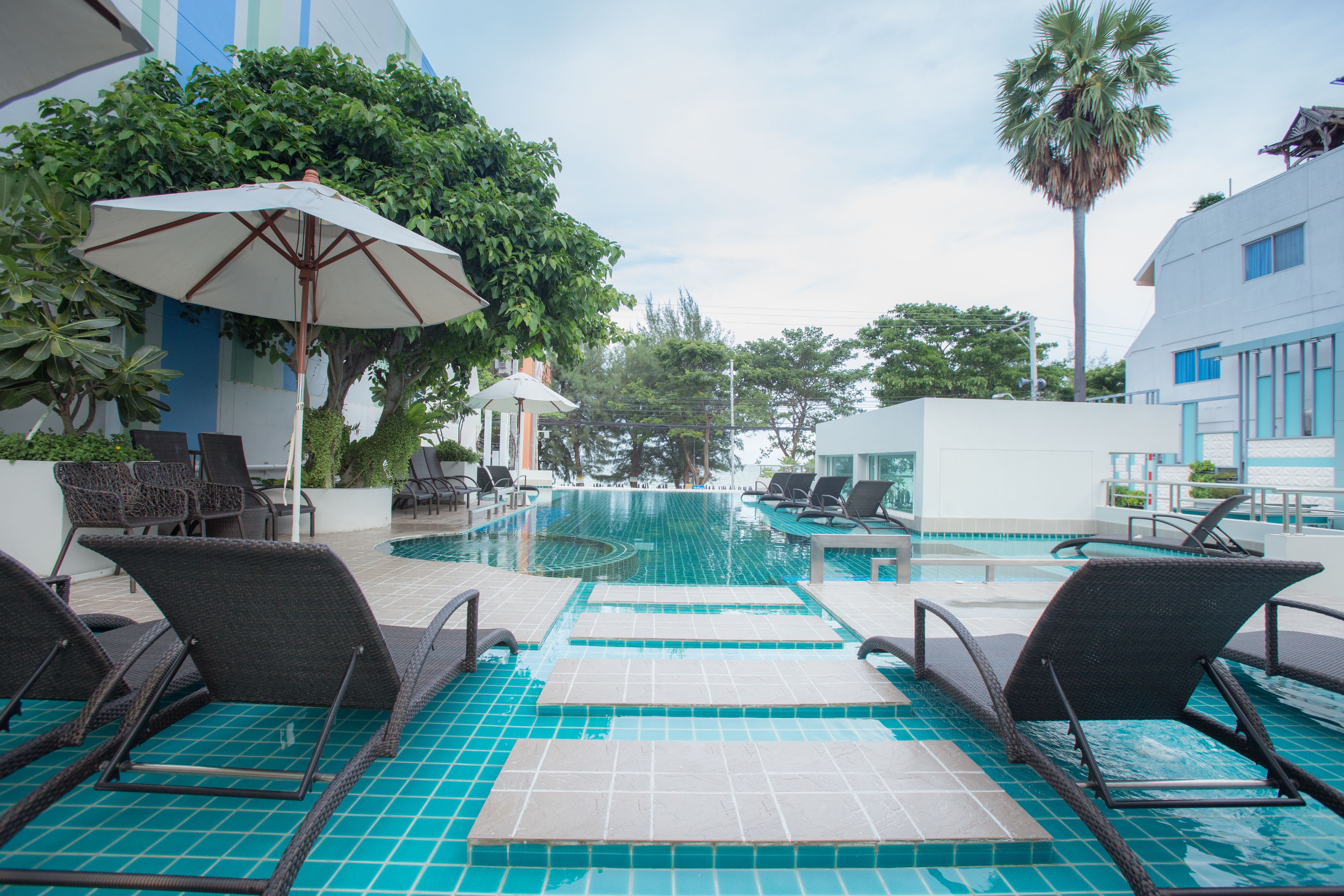 Zona de piscina con sillones reclinables y sombrillas.