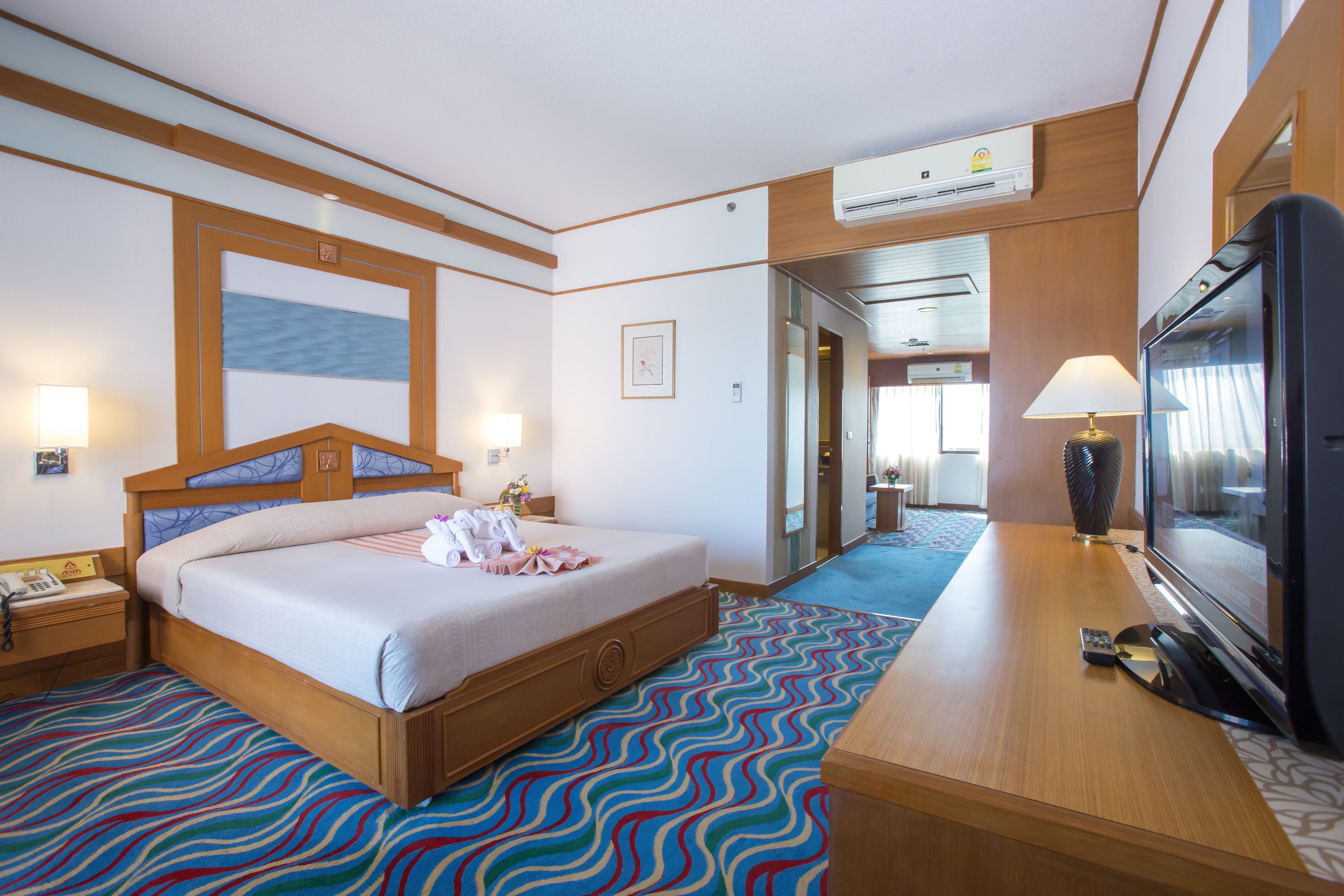 A hotel room with a bed, bedside tables, a TV, and a bathroom visible through an open door.
