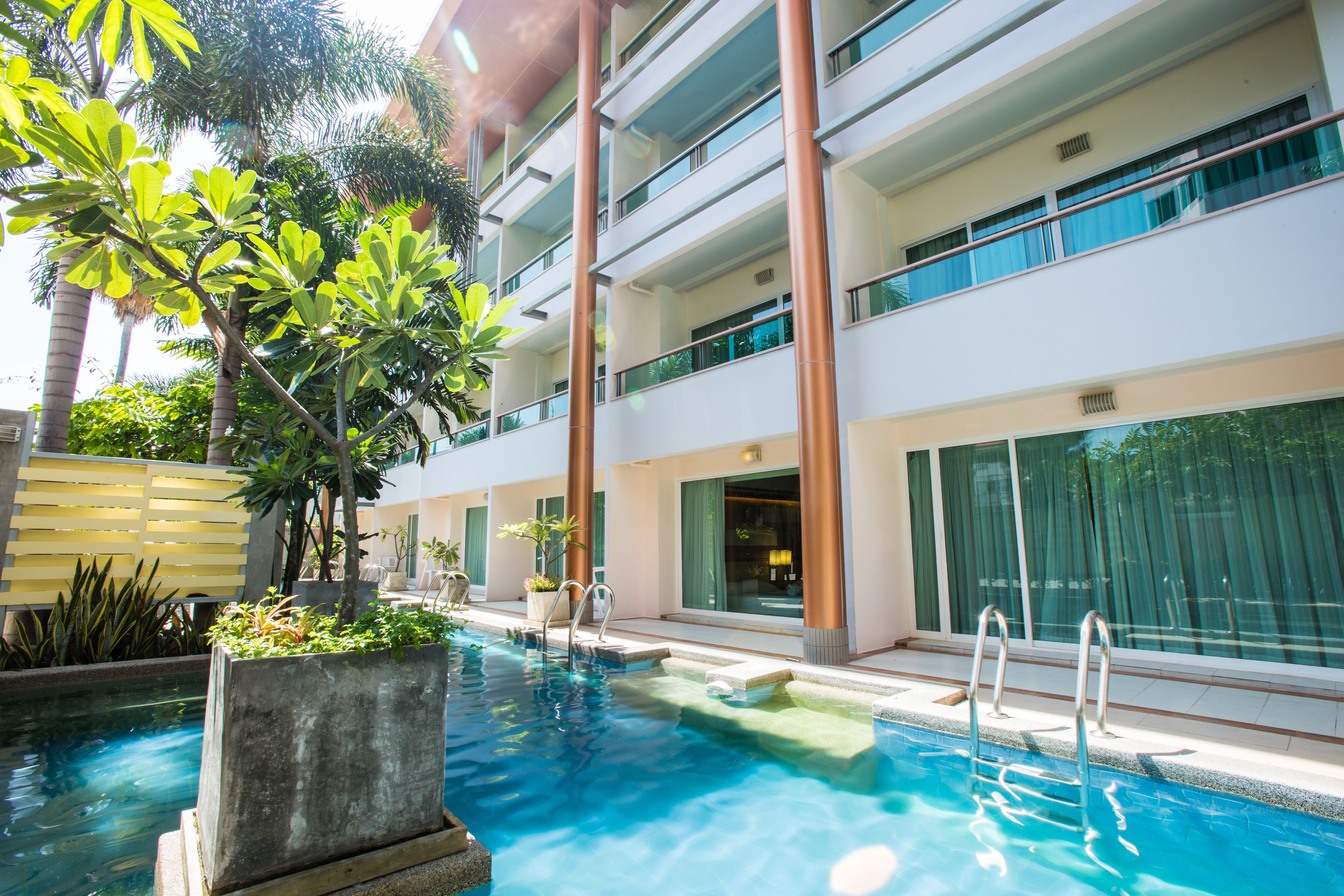 A modern hotel with a swimming pool, multiple balconies, and lush greenery.