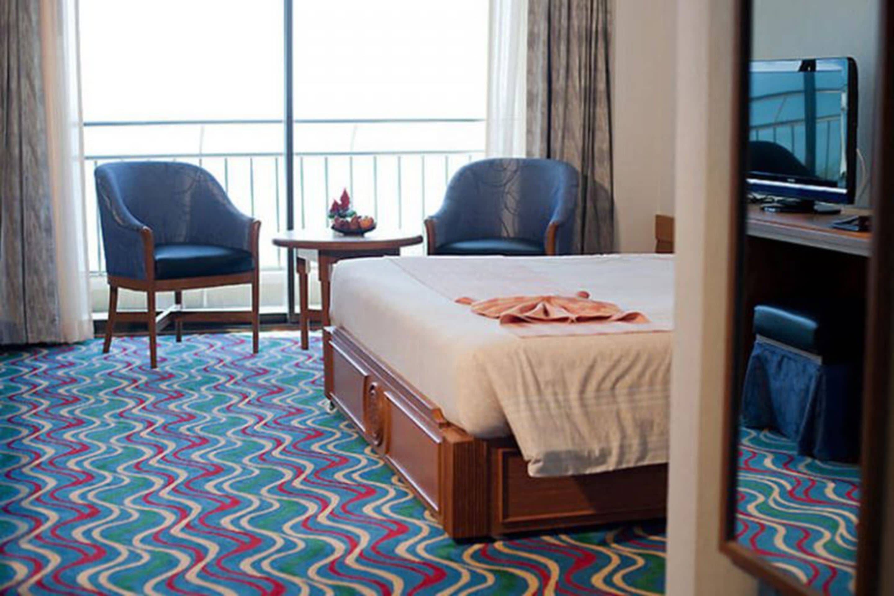 A hotel room with a bed, two chairs, a small table, and a large window with curtains.