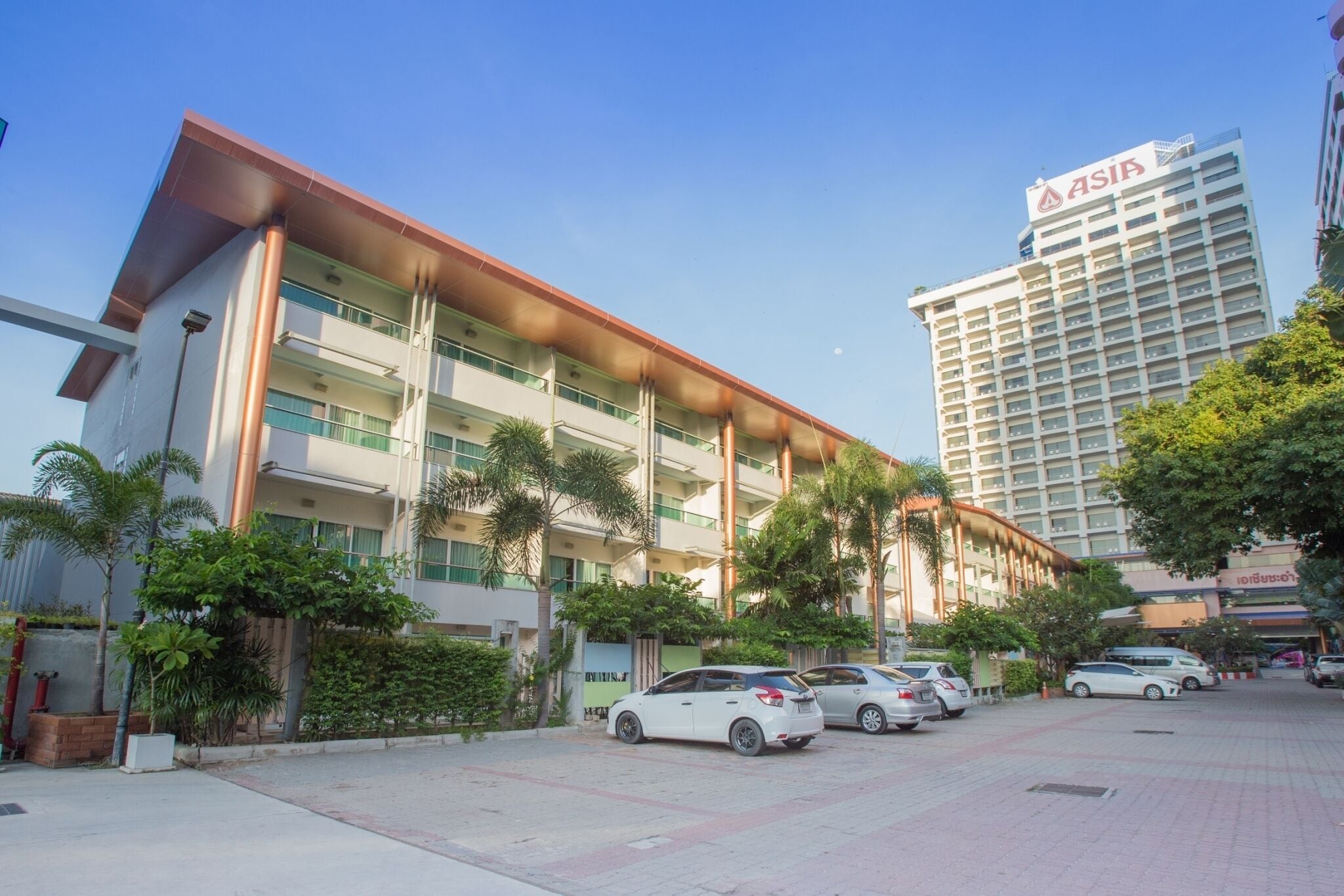 Un edificio de varios pisos con un letrero llamativo de ASIA, rodeado de coches estacionados y palmeras.