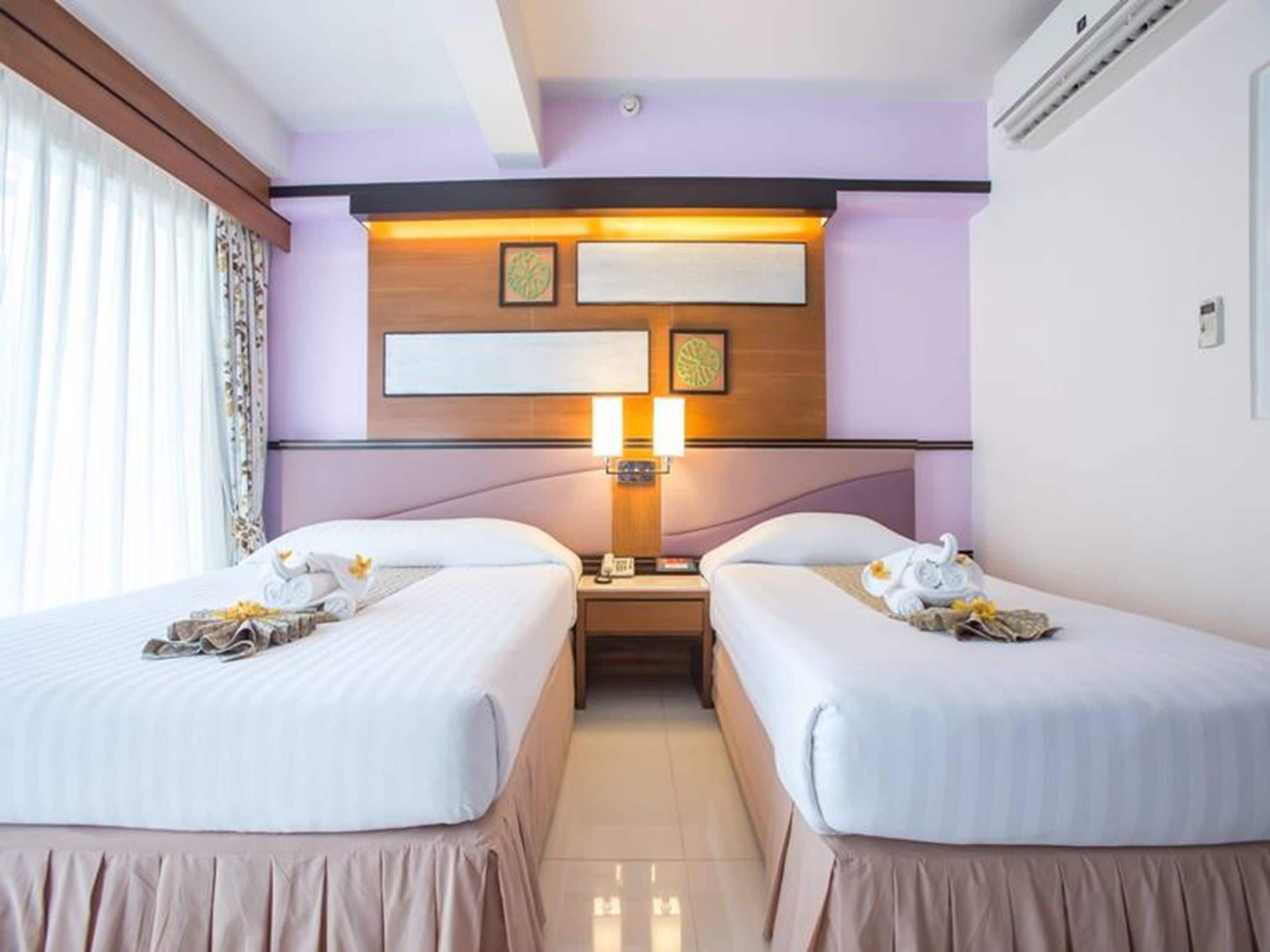A hotel room with two beds, a nightstand, a lamp, and a wall-mounted artwork.