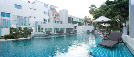 A swimming pool with lounge chairs and umbrellas, surrounded by modern buildings with balconies and windows.