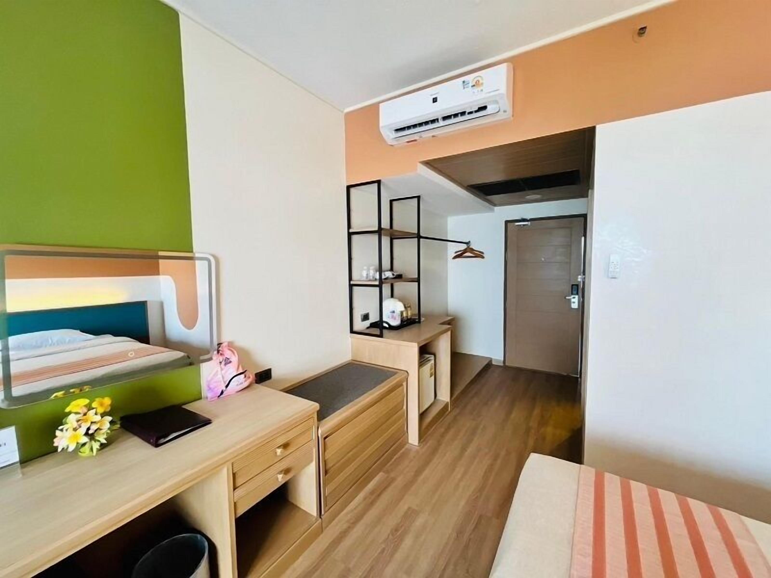 Une chambre d’hôtel de taille réduite, comprenant un lit, un bureau, une chaise, une armoire et un appareil de climatisation.