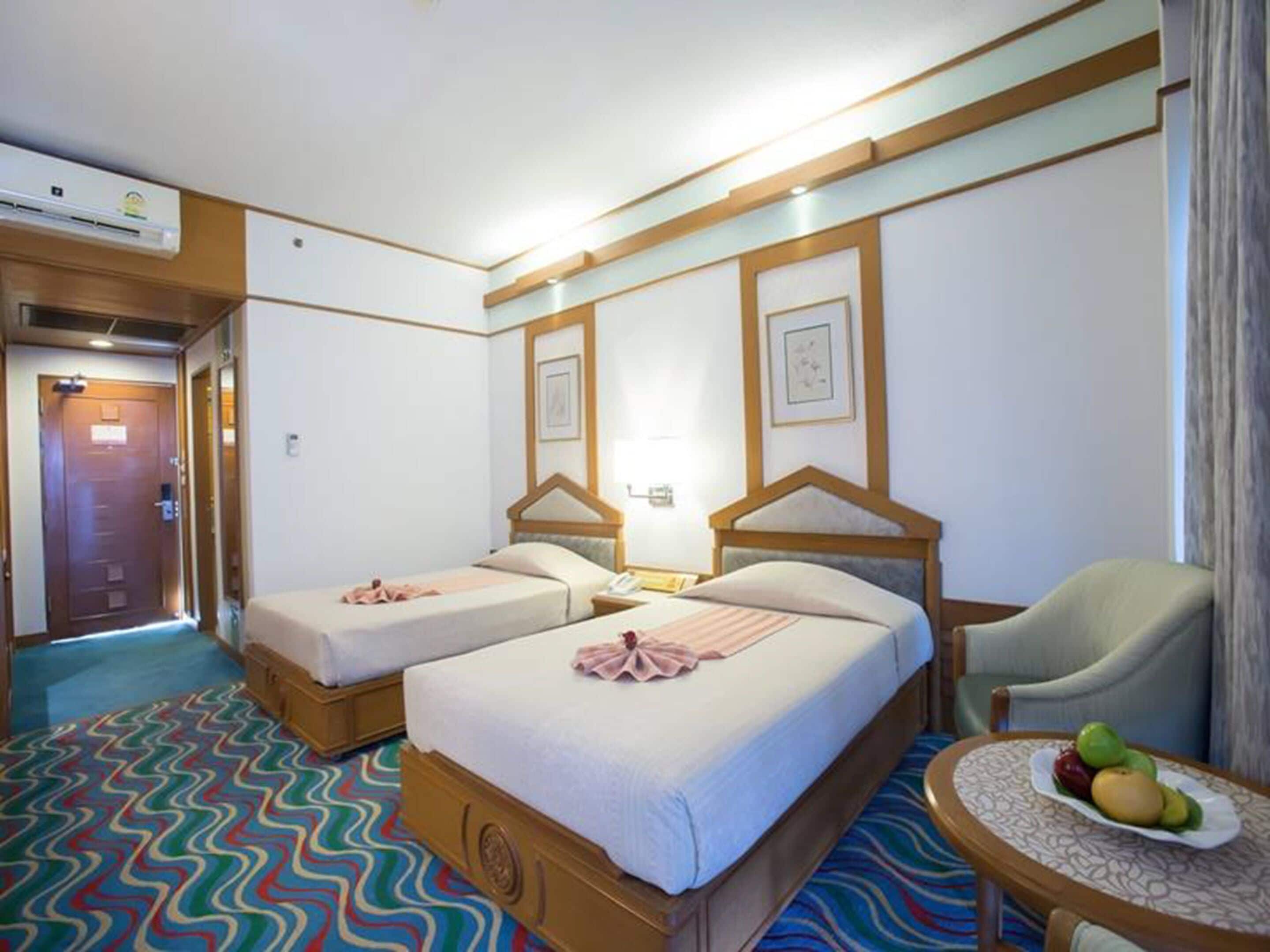 Habitación de hotel con dos camas, una silla y una mesita con fruta.
