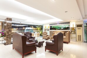 Een moderne lobby met leren banken, een marmeren pilaar en uitzicht op de straat.