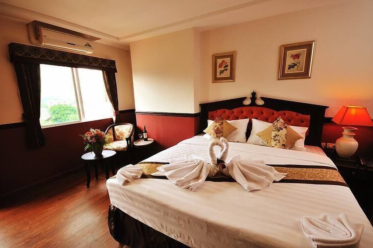 Hotelkamer met een groot bed, een kleine tafel met een bloevas en een raam met gordijnen.