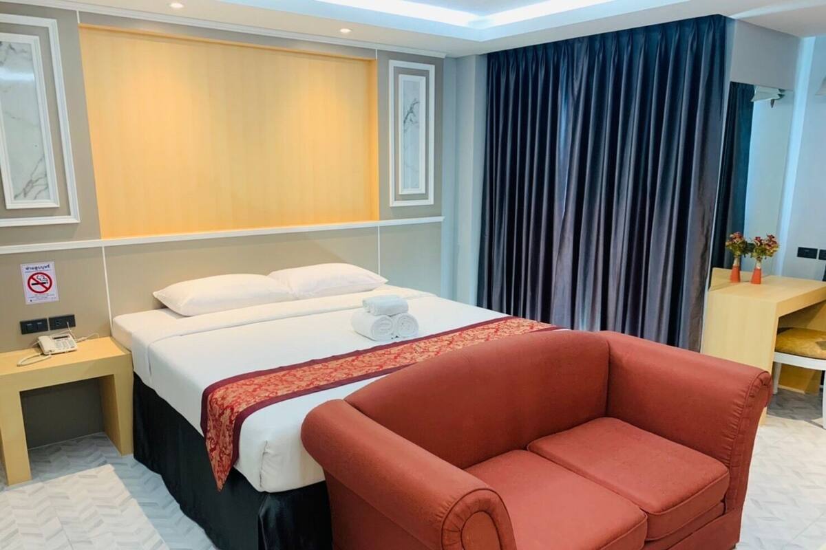 Een hotelkamer met een bed, een rode bank, een nachtkastje met een telefoon en een bureau met een bloemenvaas.